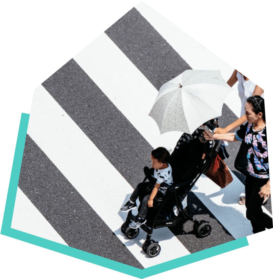 Two women crossing a cross walk, one holding an umbrella, and the other pushing a baby in a stroller.